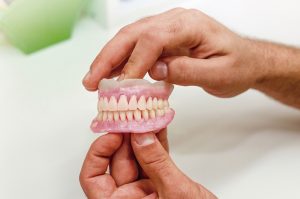 Na imagem uma pessoa segura em suas mãos uma prótese de arcada dentária. É possível ver todos os dentes do lado esquerdo do objeto.